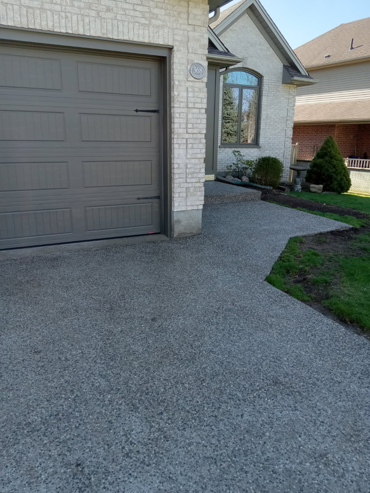 An exposed aggregate concrete driveway with walkway and front porch performed by Ultimate Touch Concrete, a concrete company in London Ontario specializing in both residential and commercial concrete services.